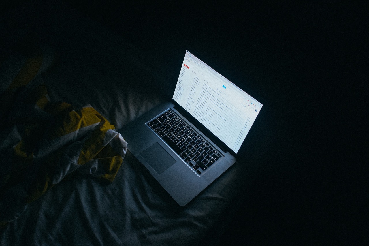 Illuminated computer opened to Gmail sitting on bed