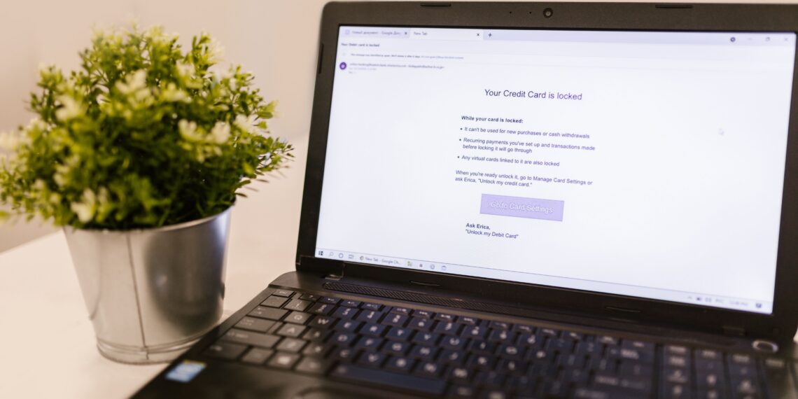 A laptop on a desk showing a simulated phishing email notification about a locked credit card, used as a visual example of phishing threats and the need for effective merchant fraud monitoring systems.
