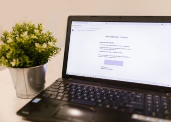 A laptop on a desk showing a simulated phishing email notification about a locked credit card, used as a visual example of phishing threats and the need for effective merchant fraud monitoring systems.
