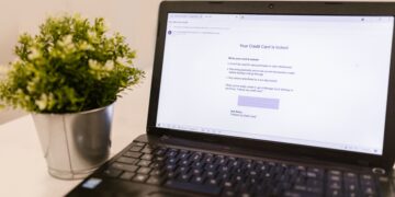 A laptop on a desk showing a simulated phishing email notification about a locked credit card, used as a visual example of phishing threats and the need for effective merchant fraud monitoring systems.