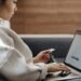 A woman sitting on a sofa while typing on her laptop and holding a credit card, illustrating the secure online login and verification processes discussed in "What Is Multi-Factor Authentication?".