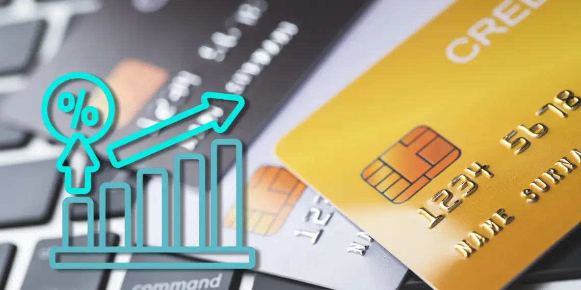 Close-up shot of multiple credit cards scattered over a black laptop keyboard. A prominent gold credit card sits in the foreground. Layered on top of the left side is a bright cyan line icon showing a rising bar graph with a percentage sign and an upward-pointing arrow, symbolizing an increase in rates or credit card fraud statistics.