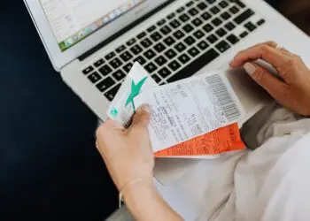 A person seated with a laptop reconciles their spending, holding a debit card alongside printed receipts while checking transaction records on screen — an everyday moment of expense-tracking that can also help spot signs of first-party fraud, such as disputing legitimate purchases.