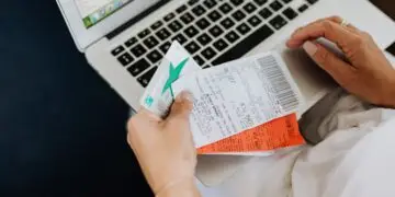 A person seated with a laptop reconciles their spending, holding a debit card alongside printed receipts while checking transaction records on screen — an everyday moment of expense-tracking that can also help spot signs of first-party fraud, such as disputing legitimate purchases.
