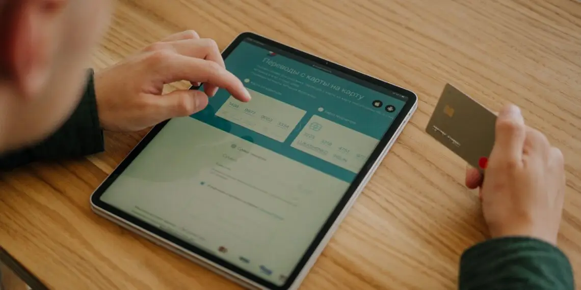 Person entering credit card details on a tablet to complete an online money transfer, illustrating the card-not-present transactions that make eCommerce fraud prevention essential for online merchants.
