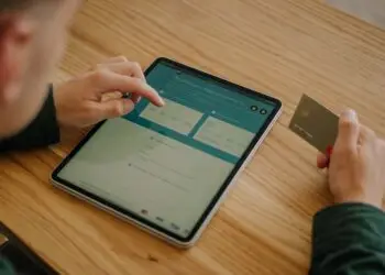 Person entering credit card details on a tablet to complete an online money transfer, illustrating the card-not-present transactions that make eCommerce fraud prevention essential for online merchants.