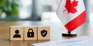 Stock photo of three wooden blocks with icons of a person, padlock, and checkmark shield, beside a small Canadian flag and a document titled “Fraud Prevention” with a pie chart, on a desk.