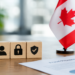 Stock photo of three wooden blocks with icons of a person, padlock, and checkmark shield, beside a small Canadian flag and a document titled “Fraud Prevention” with a pie chart, on a desk.