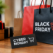 Stock photo of shopping bags labeled “Black Friday” and a “Cyber Monday” card with a shopping cart icon, beside wrapped gift boxes on a wooden table, illustrating holiday shopping sales.