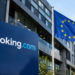 Stock photo of a blue “Booking.com” sign outside an office building, with European Union flags flying nearby against a clear sky.