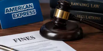 Stock photo of a judge’s gavel resting beside a document titled “Fines,” with an American Express sign and law books labeled “Banking Law” and “Regulations” in the background, illustrating regulatory fines or legal action against a financial company.