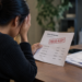 Stock photo of a distressed woman holding her head while reading a bank statement marked “Fraud Alert,” listing several pending online and card-not-present charges, with additional mail and an “Account Alert” envelope on the desk beside her.
