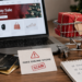 Stock photo of a laptop displaying a “Holiday Sale” shopping website beside a small shopping cart with wrapped gifts, credit cards, a notepad listing “Holiday Gifts, Online Shopping, Stay Safe,” and a warning card reading “Fake Online Store — SCAM,” illustrating holiday online shopping fraud risks.