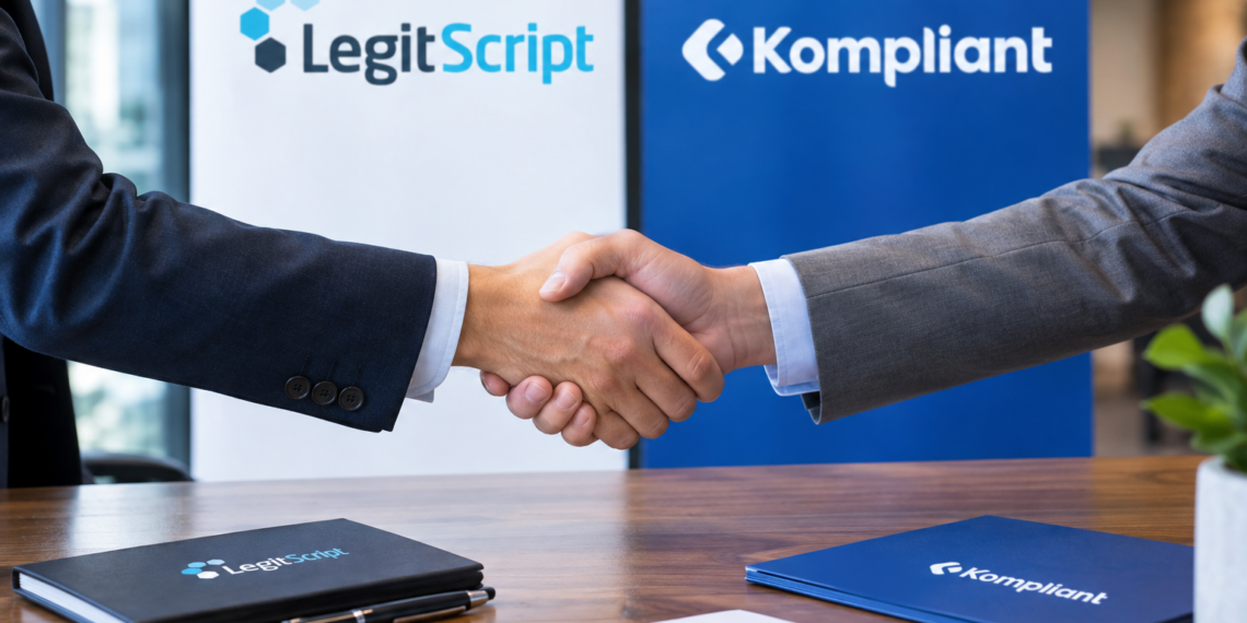 Stock photo of two businesspeople shaking hands over a desk, with LegitScript and Kompliant branded folders, a pen, and a signed document on the table, and company logo banners in the background, symbolizing a partnership between the two compliance companies.