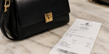 Stock photo of a black leather handbag with a gold clasp beside a Tory Burch store receipt showing the purchase of a “Perry Small Triple-Compartment Tote” for $498.00, with tax bringing the total to $539.12, paid by Mastercard.