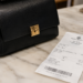 Stock photo of a black leather handbag with a gold clasp beside a Tory Burch store receipt showing the purchase of a “Perry Small Triple-Compartment Tote” for $498.00, with tax bringing the total to $539.12, paid by Mastercard.