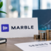 Marble logo sign beside a placard reading 'Series A €6.5M ($7.3M)' with stacks of gold coins on an office desk.