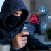 Stock photo of a person wearing a dark hoodie and face mask holding a credit card while working on a laptop, with digital icons of a hacker, an unlocked padlock, a credit card, and stacked coins overlaid beside them, symbolizing card fraud or identity theft.