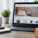 Stock photo of a laptop displaying the “LuxeStyle” fashion e-commerce website with a “Timeless Style, Modern Living” banner and a featured collection of handbags, sneakers, a watch, and sunglasses, on a desk with a coffee mug, plant, notebook, pen, and shipping boxes.