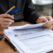 Stock photo of a person holding several credit cards while reviewing a “Government Bill” document on a desk with a calculator, pen, and notebook, illustrating bill payment or billing management.