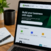 Stock photo of a laptop displaying the Shopify App Store homepage with “Build your business with apps” and popular categories like Marketing, Sales and conversion, Store design, and Customer support, beside a notebook with handwritten “App Review” checklist items (check permissions, review recent updates, confirm developer), a pen, mug, and plant.