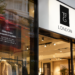 TFG London fashion retailer storefront featuring the brand’s black-and-white logo above glass display windows, with a red cybersecurity warning graphic stating “Online Orders Temporarily Unavailable” to represent a cyberattack disrupting online orders.